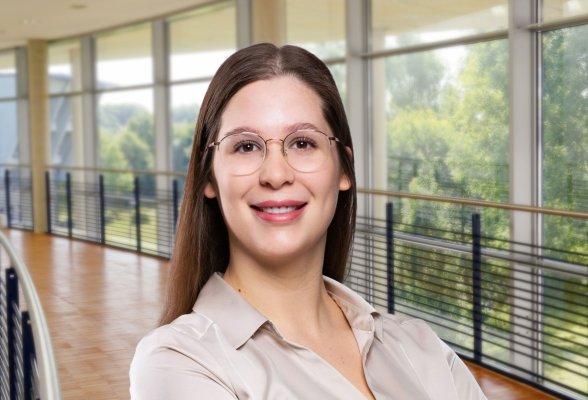 Porträtfoto: Eileen Heydenreich im audimax, sie trägt die langen, dunklen Haare offen, eine Brille und eine helle Bluse.