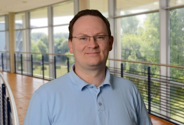 Porträtfoto: Matthias Schneider im audimax, er trägt dunkelblonde, kurze Haaare, eine unauffällige Brille und ein hellblaues Poloshirt.