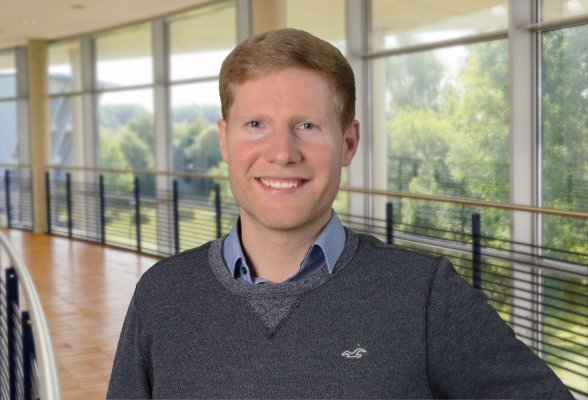 Porträtfoto: Michel Carl im audimax, er trägt dunkelblonde, kurze Haaare und ein hellblaues Hemd unter einem grauen Pullover.