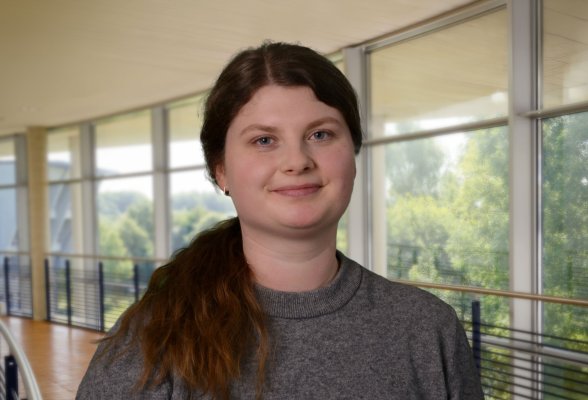 Porträtfoto: Jasmin Pohlmann im audimax, sie trägt die langen, dunkelblonden Haare zusammen gebunden, über die Schulter und einen grauen Pullover.