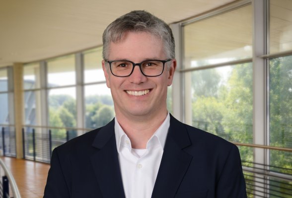 Porträtfoto: Sönke Bohm im audimax, er trägt grau-blonde, kurze Haaare, eine Brille und ein weißes Hemd unter einem schwarzen Sakko..