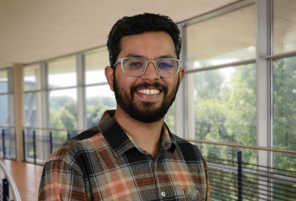 Porträtfoto: Karan Soni im audimax, er trägt dunkle, kurze Haare und Bart, eine Brille und ein kariertes Hemd.