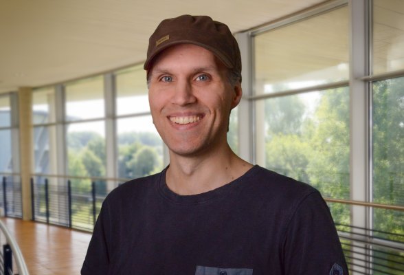 Portraitfoto von Malte Asmussen mit blaugrauem Pullover und brauner Schirmmütze im Flensburger audimax.