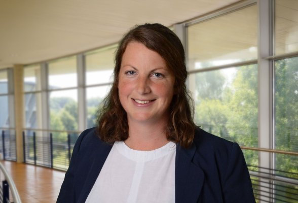 Porträtfoto: Verena Gerbaulet im audimax, sie trägt die schulterlangen dunkelblonden Haare offen, über dem weißen Oberteil trögt sie einen dunkelblauen Blazer.