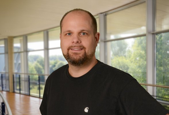 Portraitfoto: Kai Thiemann im audimax, er trägt einen Bart und ein schwarzes T-Shirt.
