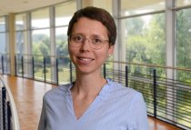 Porträtfoto: Ann-Kathrin von Hielmcrone im audimax, sie trägt kurze Haare und eine hellblaue Bluse mit dünnen, weißen Streifen.