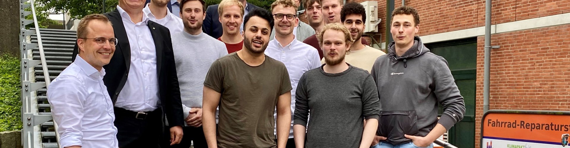 Gruppe von Studierenden und Lehrenden posieren auf einer TReppe. Sie lachen in die Kamera.
