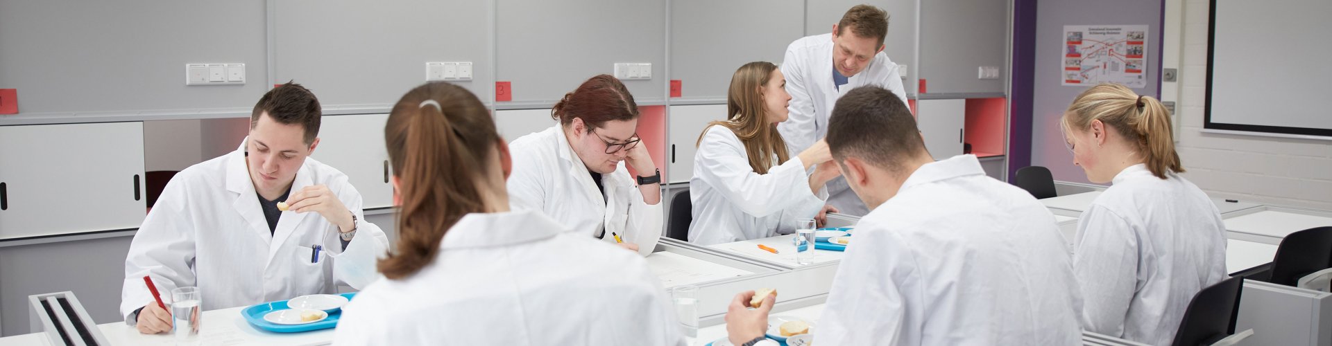 Studentin pipetiert im Labor. Sie trägt Laborkittel, Handschuhe und Schutzbrille.