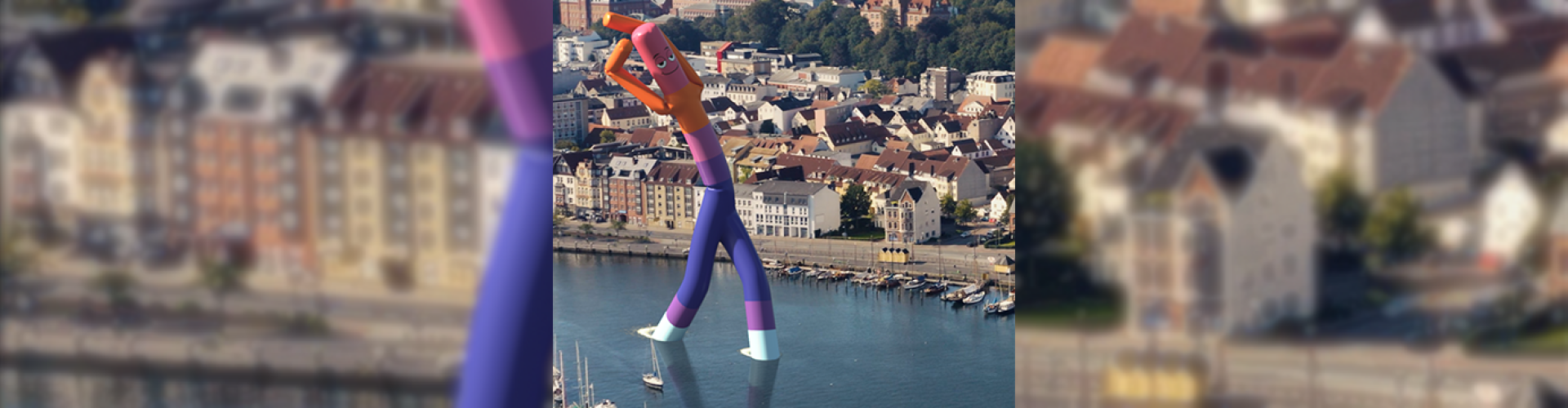 Der Flensburger Hafen aus der Vogelperspektive - im Wasser steht ein riesiges Windmännchen in den Farben der Hochschule Flensburg.