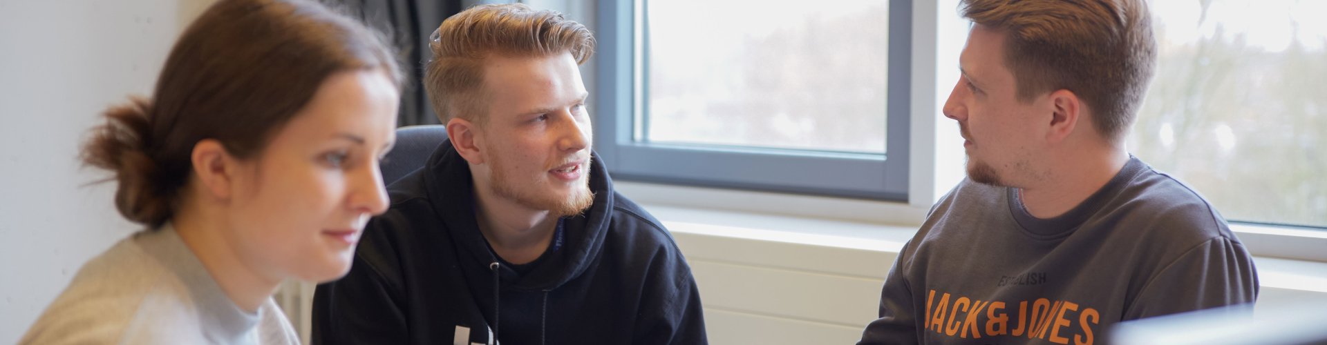 Drei Studierende sitzen zusammen, angedeutet ist ein Bildschirm zu sehen.