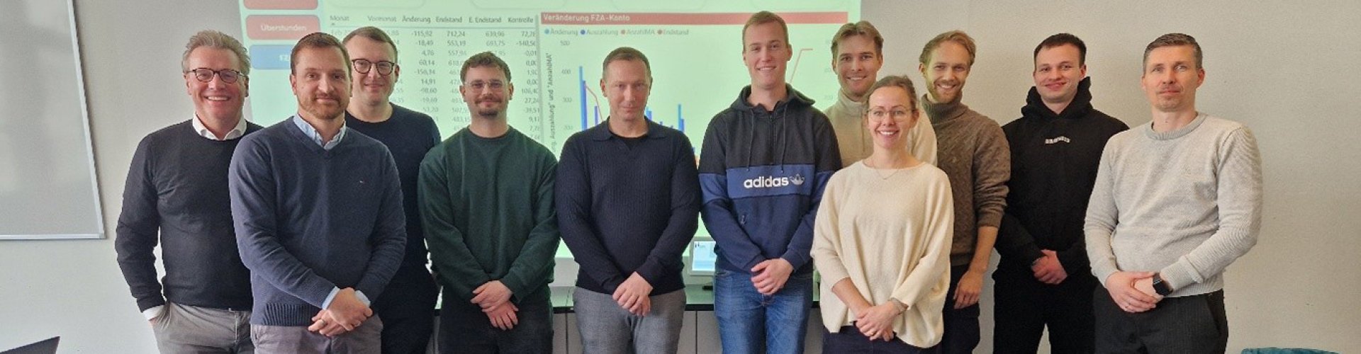 Eine Gruppe von Studierenden steht mit Vertretern der NVB und Sina Völtzer in einem Seminarraum vor einem Dashboard und lächelt in die Kamera.