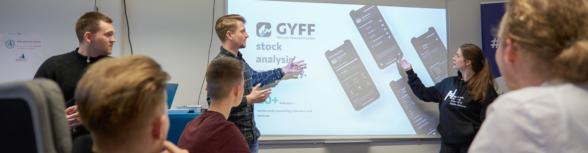 Studierende erklären etwas an einem Bildschirm, andere hören zu.