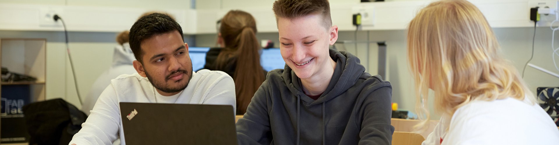 Drei Studierende sitzen in einem Labor an einem Tisch und arbeiten gemeinsam am Laptop.