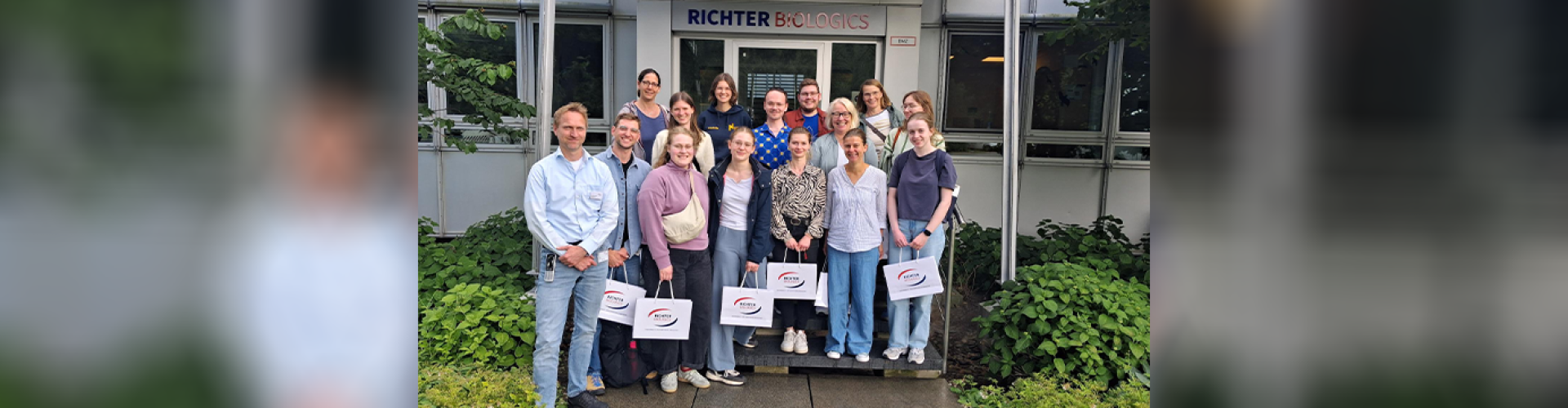 Eine Gruppe von Studierenden und Lehrenden steht lächelnd vor einem Hauseingang, über dem groß "Richter Biologics" steht.